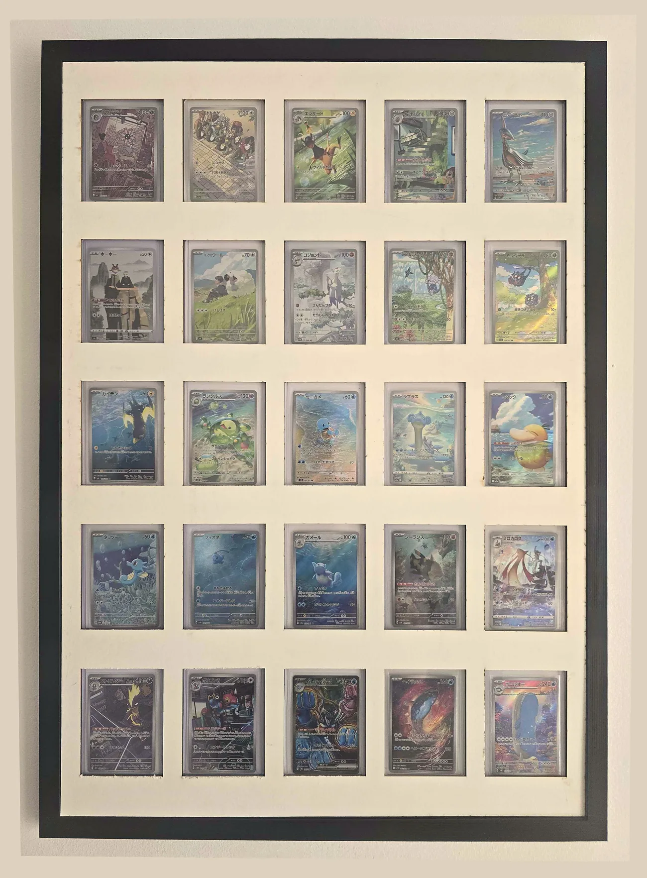 A black wall frame with an ivory window mat holding 25 trading cards in a 5 by 5 grid